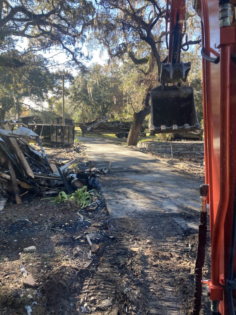Excavator removing debris from a driveway with dumpsters in the background during a property cleanout