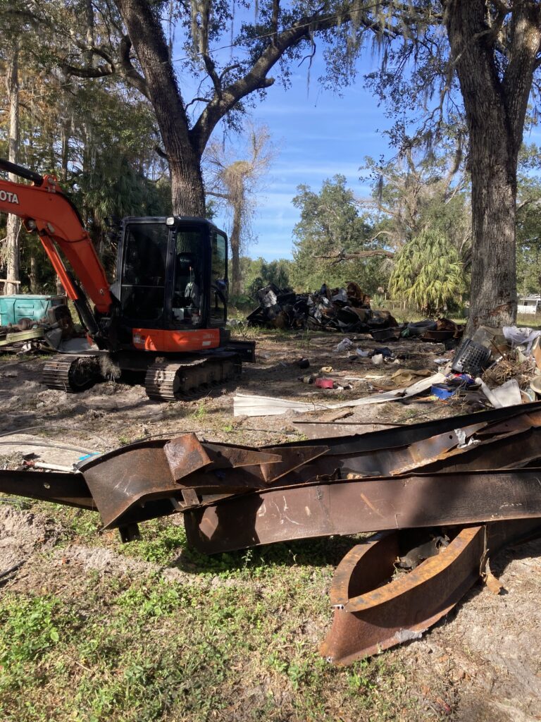 Excavator clearing large piles of scrap metal and debris during a property cleanout